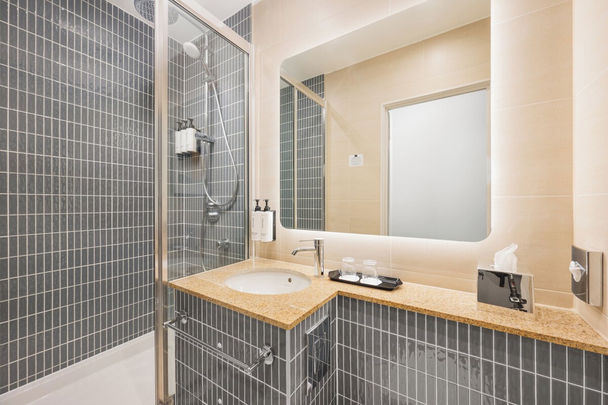 A bathroom with a sink, mirror, and shower.