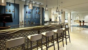 A modern bar area with a blue patterned wall, hanging pendant lights, and bar stools.