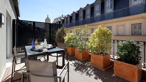 A terrace with a table set for breakfast, potted plants, and a view of the cityscape.