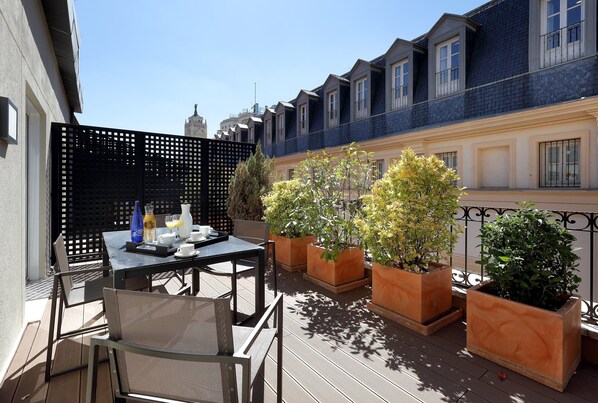 A terrace with a table set for breakfast, potted plants, and a view of the cityscape.
