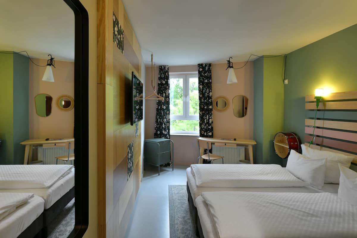 A bedroom with two beds, a mirror, a radiator, a desk with a chair, and a window with curtains.