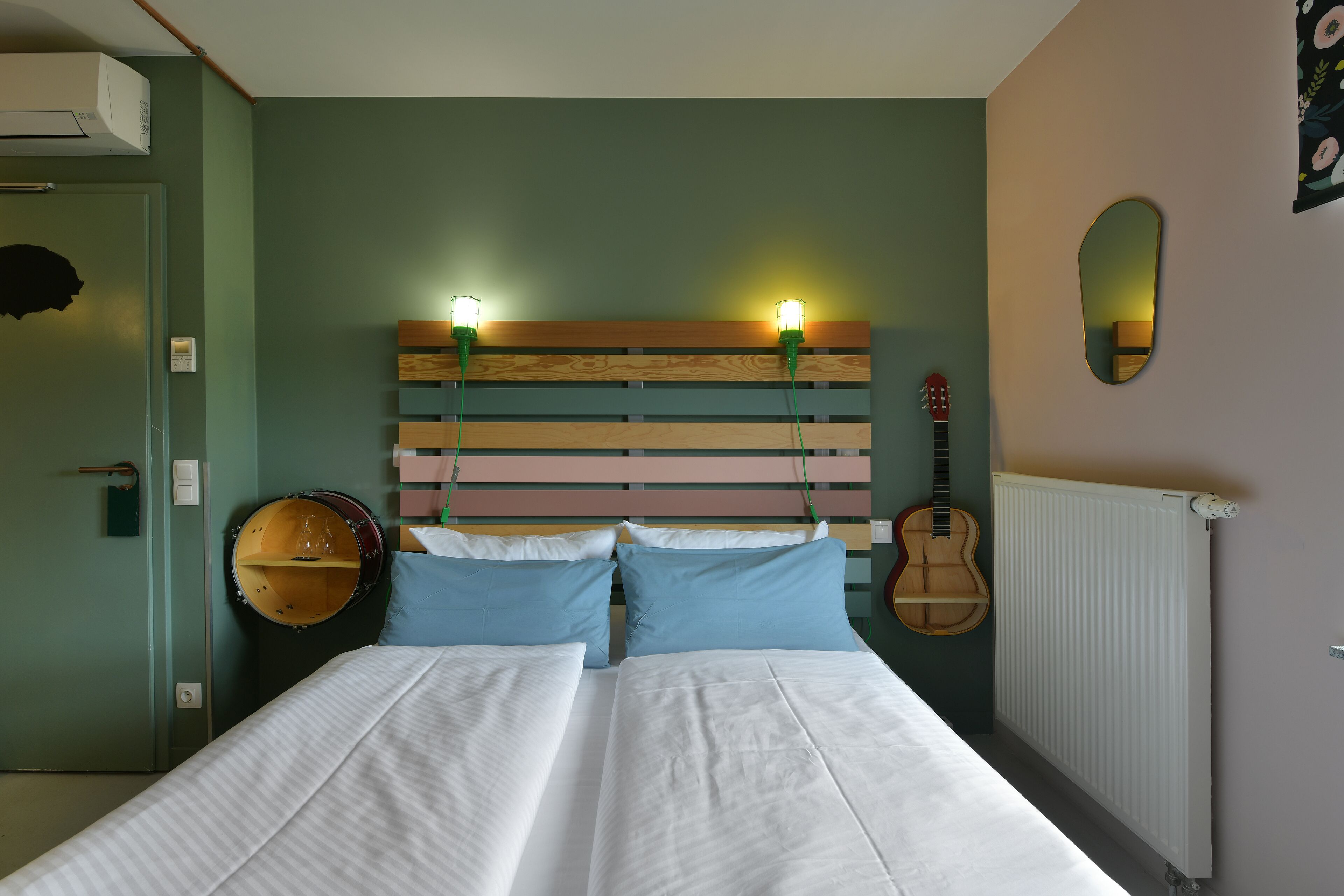 Une chambre à coucher avec un lit, une tête de lit, une guitare, un miroir et un radiateur.