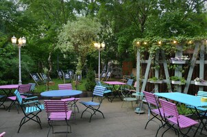 An outdoor patio with tables and chairs, surrounded by greenery and decorative lighting.