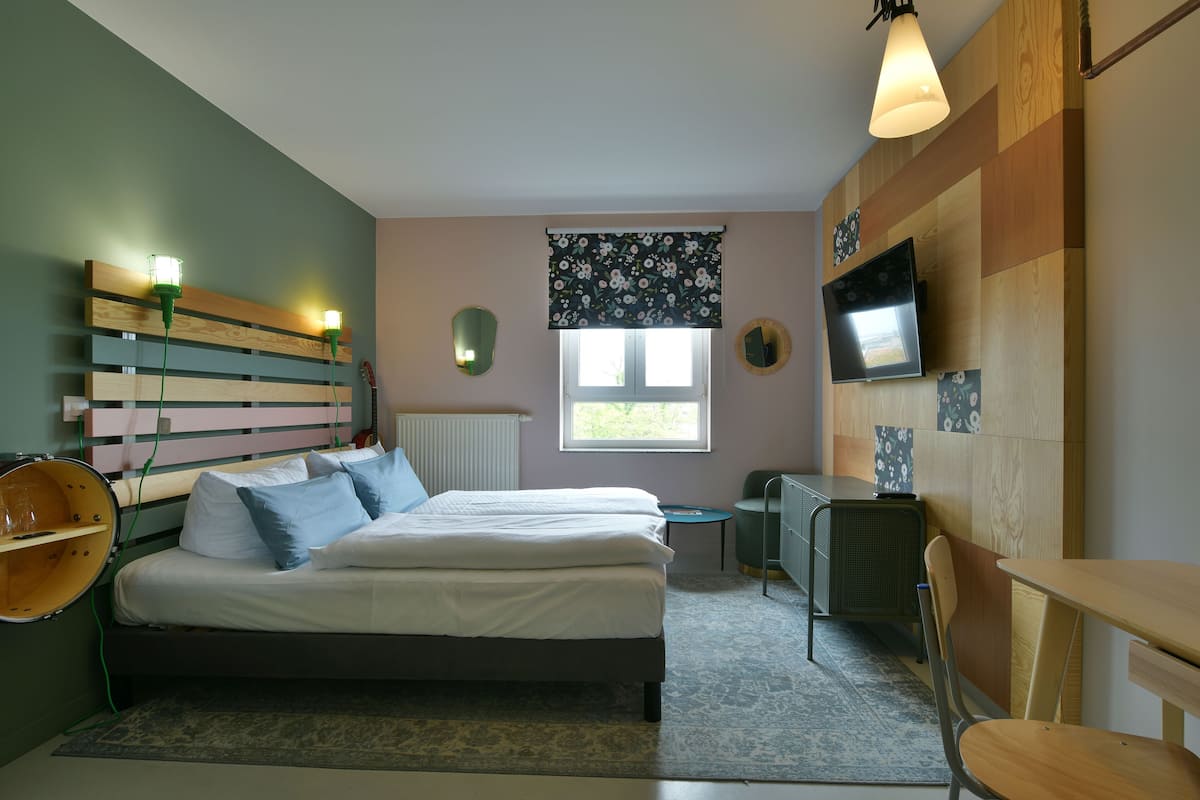 A bedroom with a bed, bedside tables, a desk, a chair, a television, and a window.