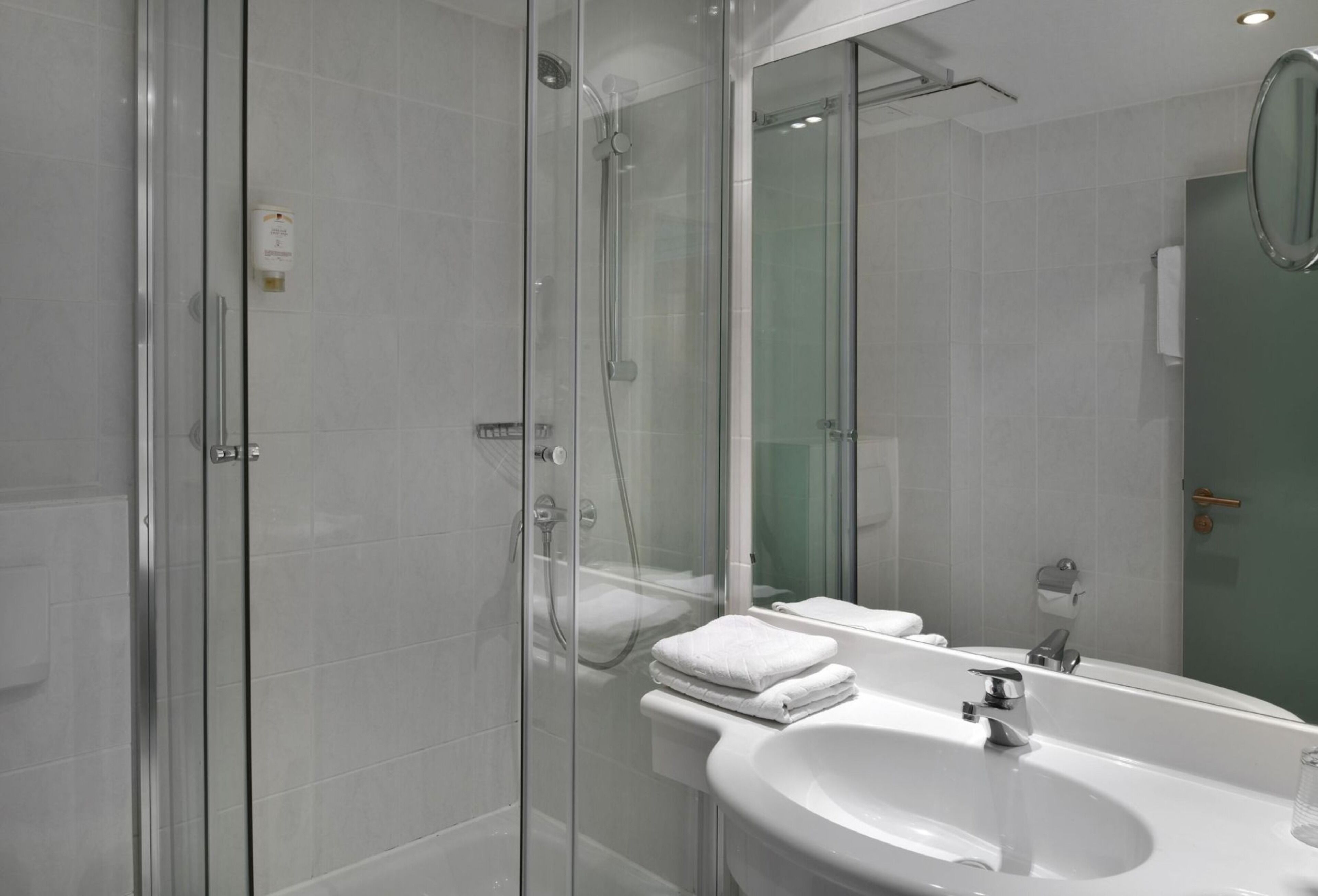 Un baño moderno con ducha envuelta en vidrio, un lavabo blanco y un espejo grande.