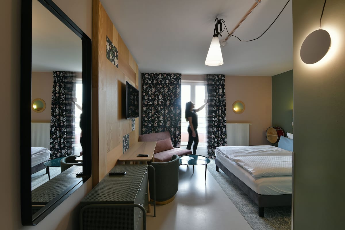 A hotel room with a bed, a desk, a chair, a sofa, a mirror, and a television.