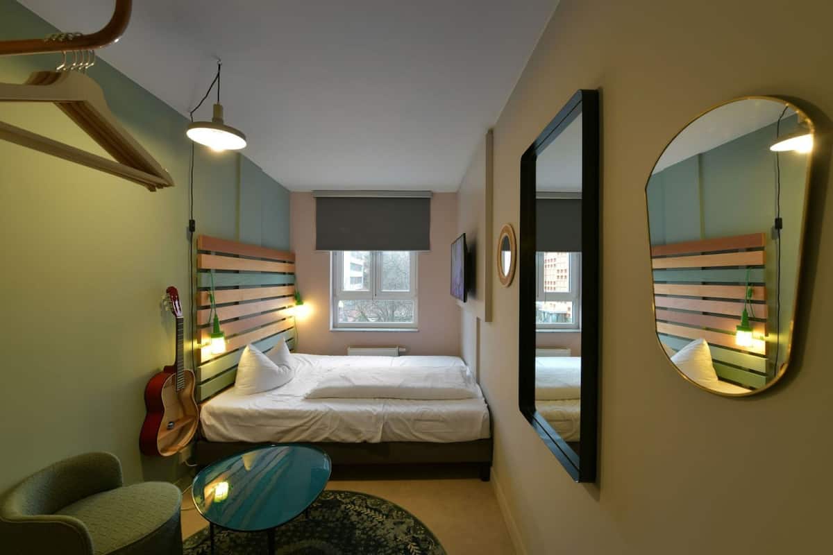 A bedroom with a bed, a hanging guitar, a round table, and a mirror.