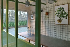 A room with a view of a garden, a table with bottles, a potted plant, and a framed picture on the wall. - Hotel BIRGIT Berlin Mitte (Berlin)