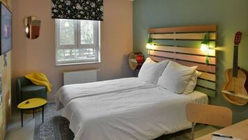 Une chambre à coucher avec un lit, une chaise, une table, une guitare et une fenêtre avec un radiateur.