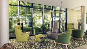 Un área de descanso moderna con ventanas amplias, sillones tapizados en verde, una zona de estar central y un piso con estampado.
