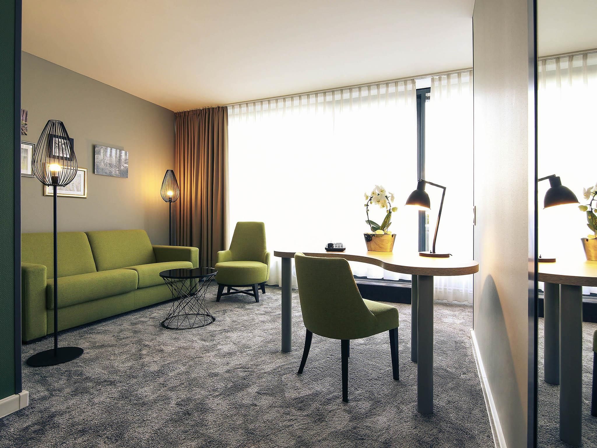 Ein modernes Wohnzimmer mit einem grünen Sofa, zwei Sesseln, einem Couchtisch und einem Esstisch mit einer Lampe.