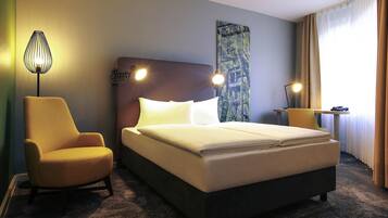 Ein Hotelzimmer mit Bett, Sessel, Lampe und einem Bild an der Wand.
