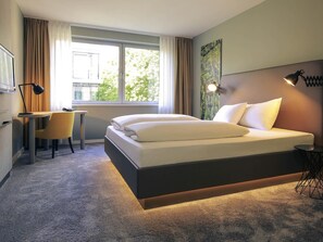 Habitación de hotel con cama, escritorio, silla y un ventanal con cortinas.