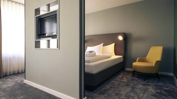 Ein Hotelzimmer mit Bett, Wandfernseher, Sessel und Teppichboden.