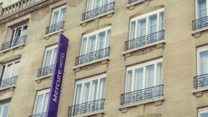 Un edificio con múltiples ventanas y balcones, un llamativo letrero púrpura que indica un hotel, y detalles arquitectónicos de estilo clásico.