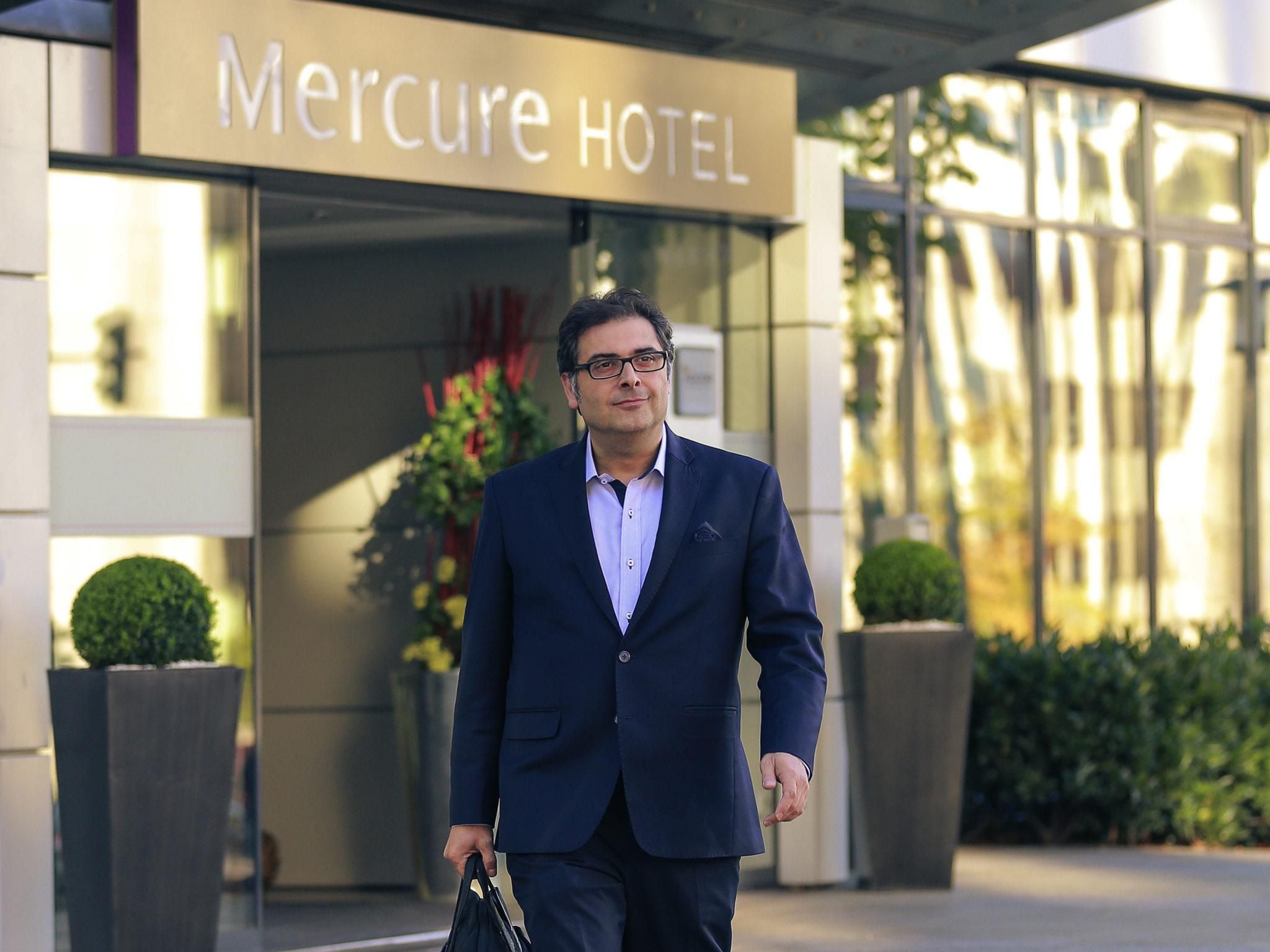 A man in a dark suit walking towards the Mercure Hotel entrance.