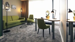 Una sala de estar moderna con un sofá verde, dos sillones, una mesa de centro y una mesa de comedor con una lámpara.