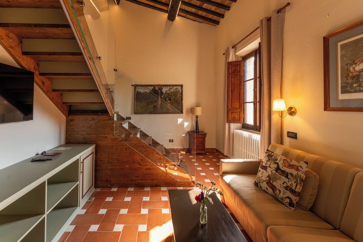 Una habitació amb una escala, un sofà, una taula amb flors i una làmpada.