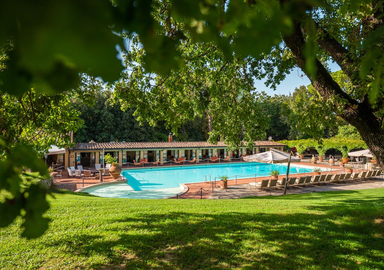 Un espace piscine avec des chaises longues et un bâtiment doté d’un toit en tuiles.
