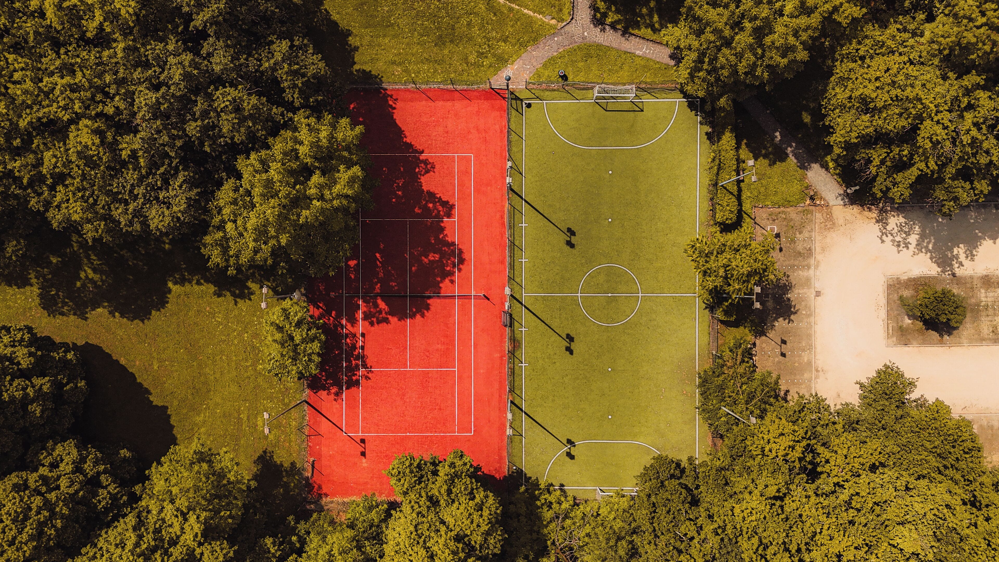 Vista aérea de un campo deportivo con una zona de juego roja y verde, rodeado de árboles.