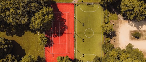 Vista aérea de un campo deportivo con una zona de juego roja y verde, rodeado de árboles.