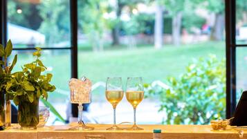 Zona de bar con vasos y botellas, una planta en maceta y vistas al verdor exterior.
