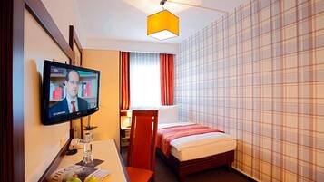 Ein Hotelzimmer mit Bett, Schreibtisch mit Computer, Fernseher und Fenster mit Vorhängen.