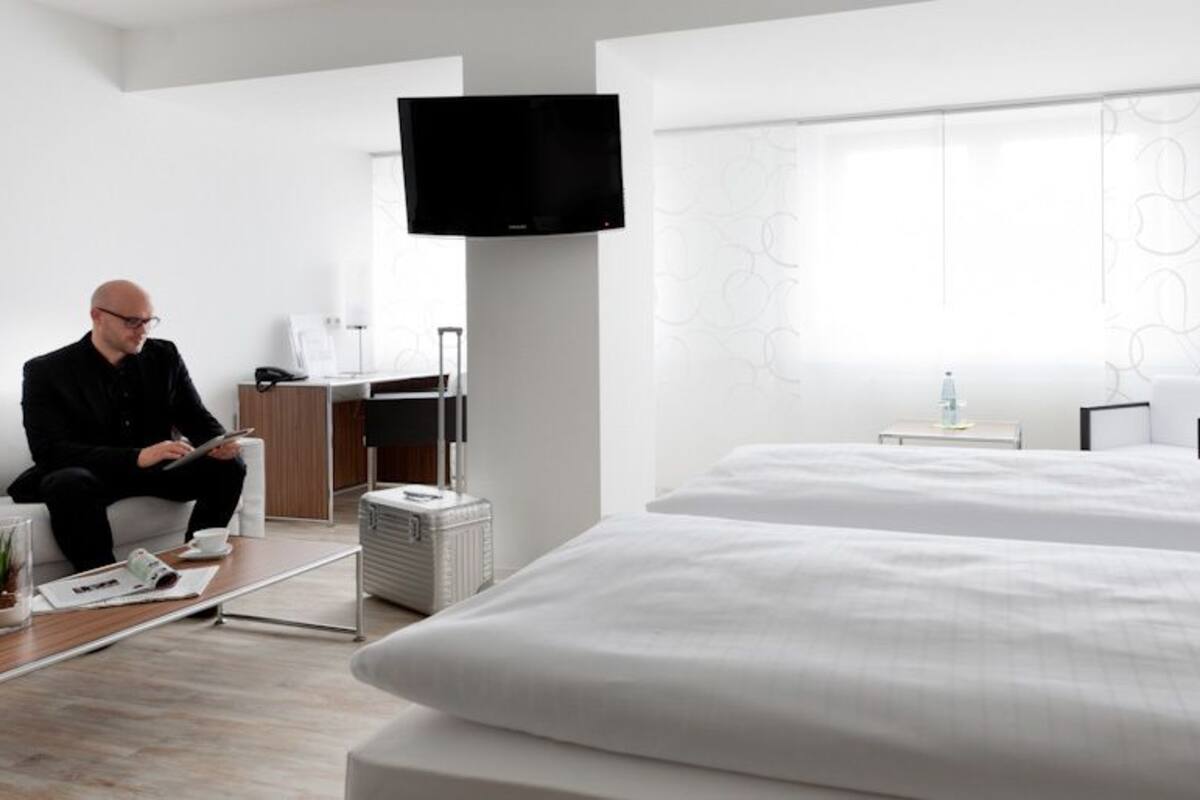 Une chambre d’hôtel moderne équipée d’un grand lit, d’un canapé, d’une télévision à écran plat et d’un bureau avec un ordinateur.