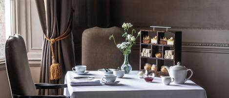A dining table with a white tablecloth, a vase with flowers, a tea set, and a dessert display.