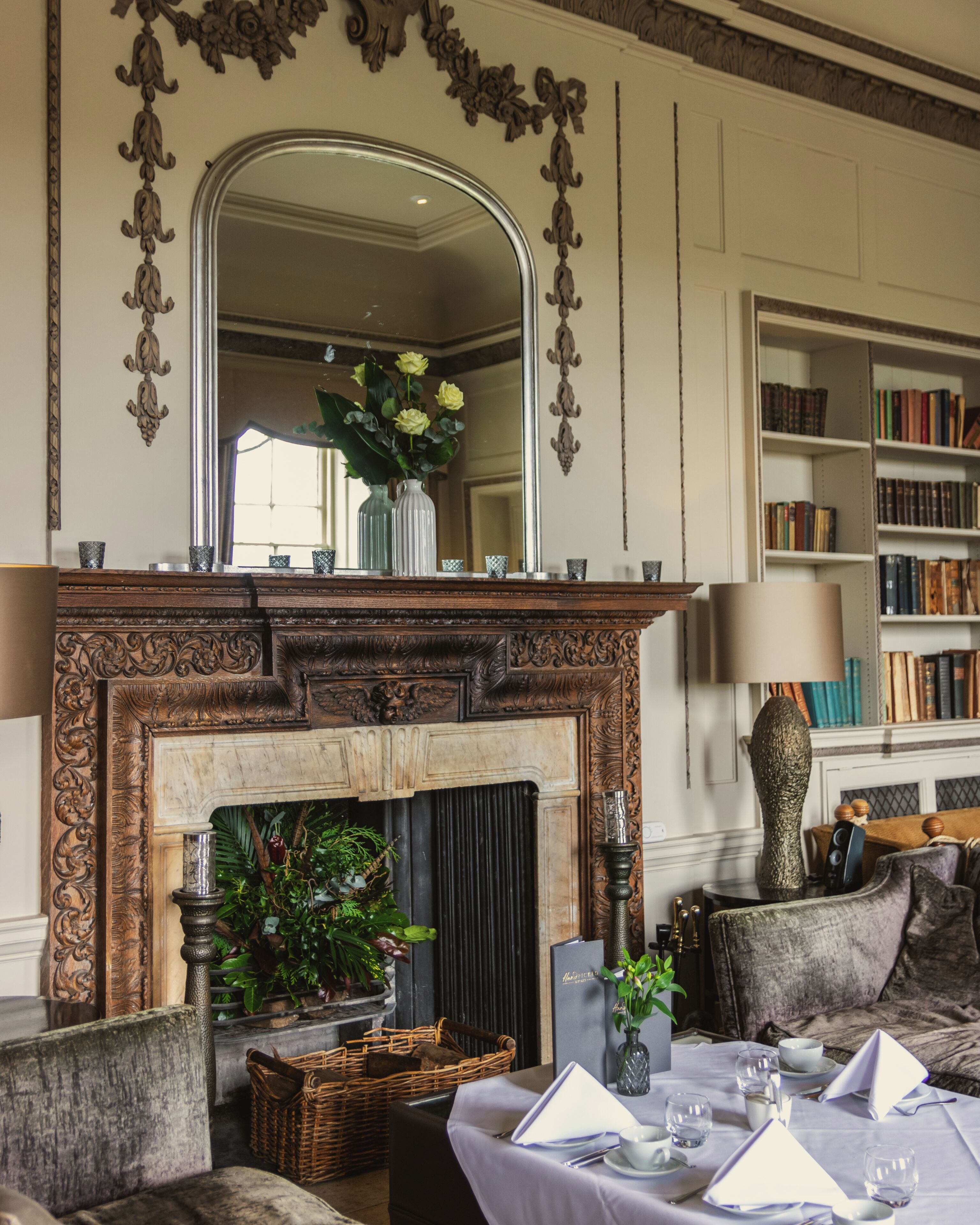A room with a fireplace, a mirror, a bookshelf, and a dining area set for a meal.
