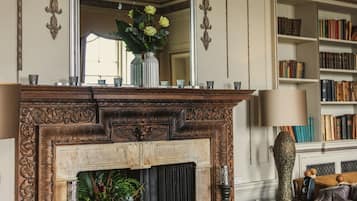 A room with a fireplace, a mirror, a bookshelf, and a dining area set for a meal.