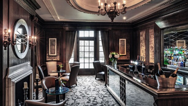 A luxurious bar area with a chandelier, bar stools, and a wine cooler. - Wood Hall Hotel and Spa (Wetherby)