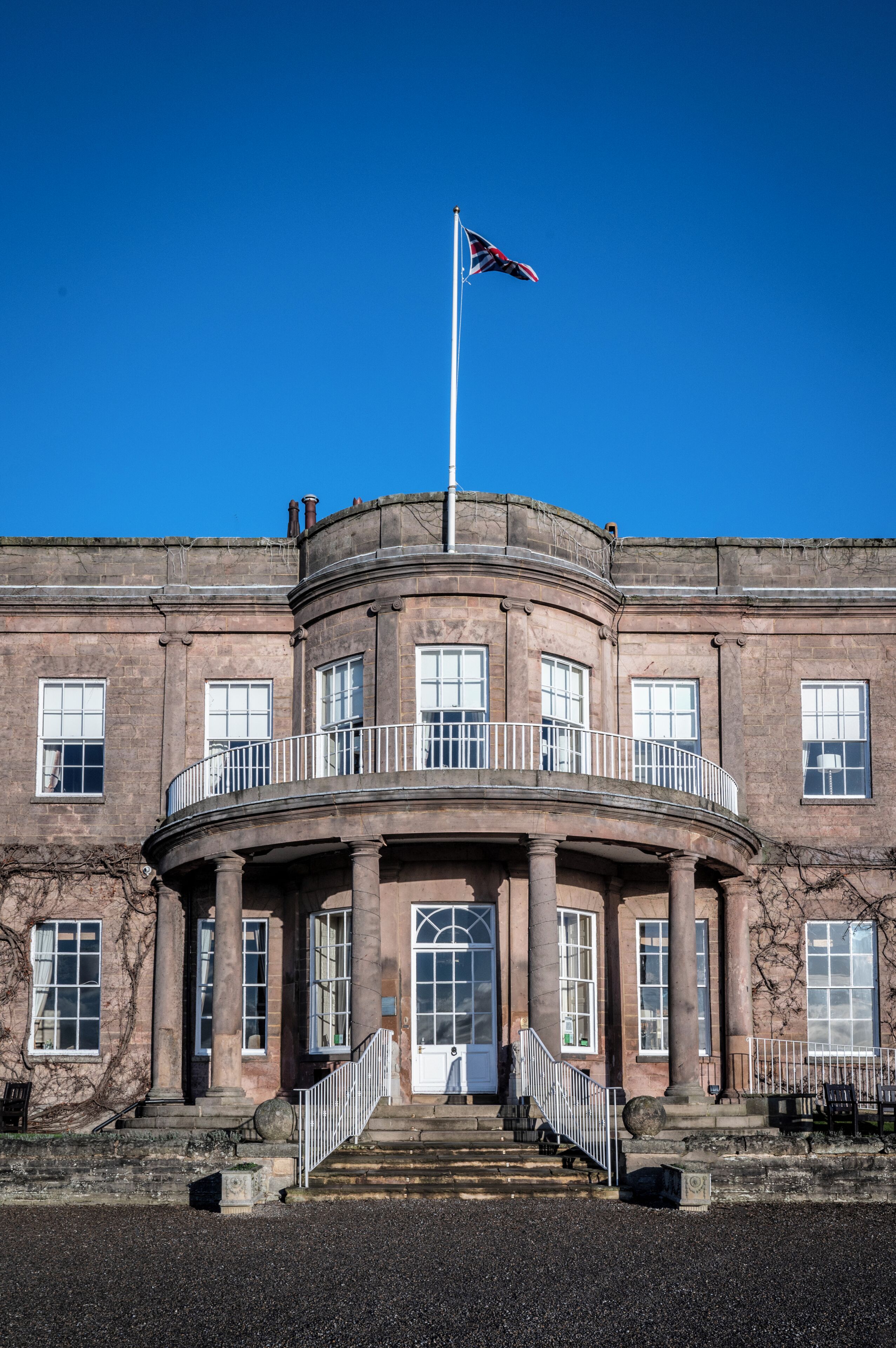 Un bâtiment historique doté d’une entrée centrale, d’un mât pour drapeau et d’un balcon circulaire.