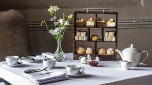 A dining table with a tea set, a vase of flowers, and a display of pastries and desserts. - Wood Hall Hotel and Spa (Wetherby)