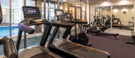 A gym with treadmills, exercise bikes, and a pool area.