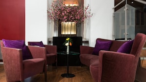 A modern room with two red upholstered chairs, a small round table, and a decorative vase with flowers. - Leonardo Hotel Frankfurt City Center (Frankfurt)