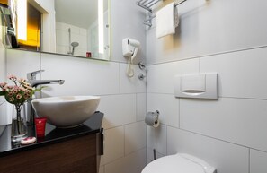 A modern bathroom with a large white sink, a handheld hair dryer, a towel rack, and a toilet. - Leonardo Hotel Frankfurt City Center (Frankfurt)