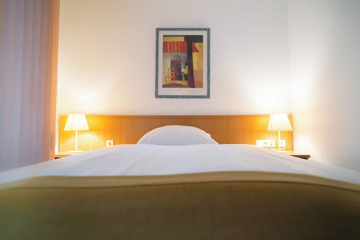 Une chambre d’hôtel avec un lit soigneusement fait, deux lampes de chevet et une œuvre d’art encadrée au mur.