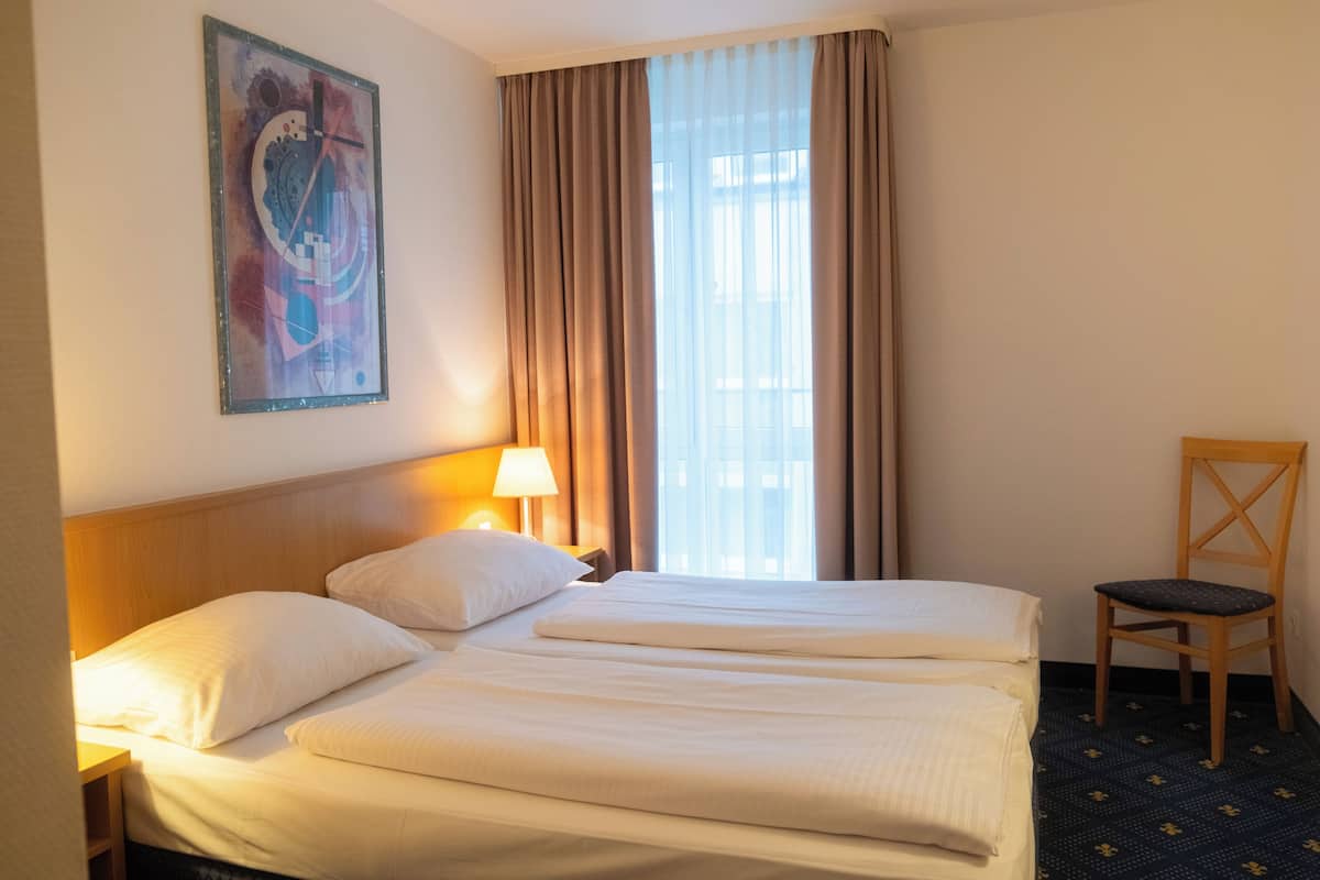 Une chambre d’hôtel avec deux lits, une table de chevet avec une lampe, une chaise et un grand tableau abstrait accroché au mur.