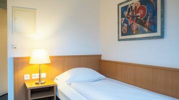 A hotel room with a bed, a nightstand with a lamp, a painting on the wall, and a power outlet.