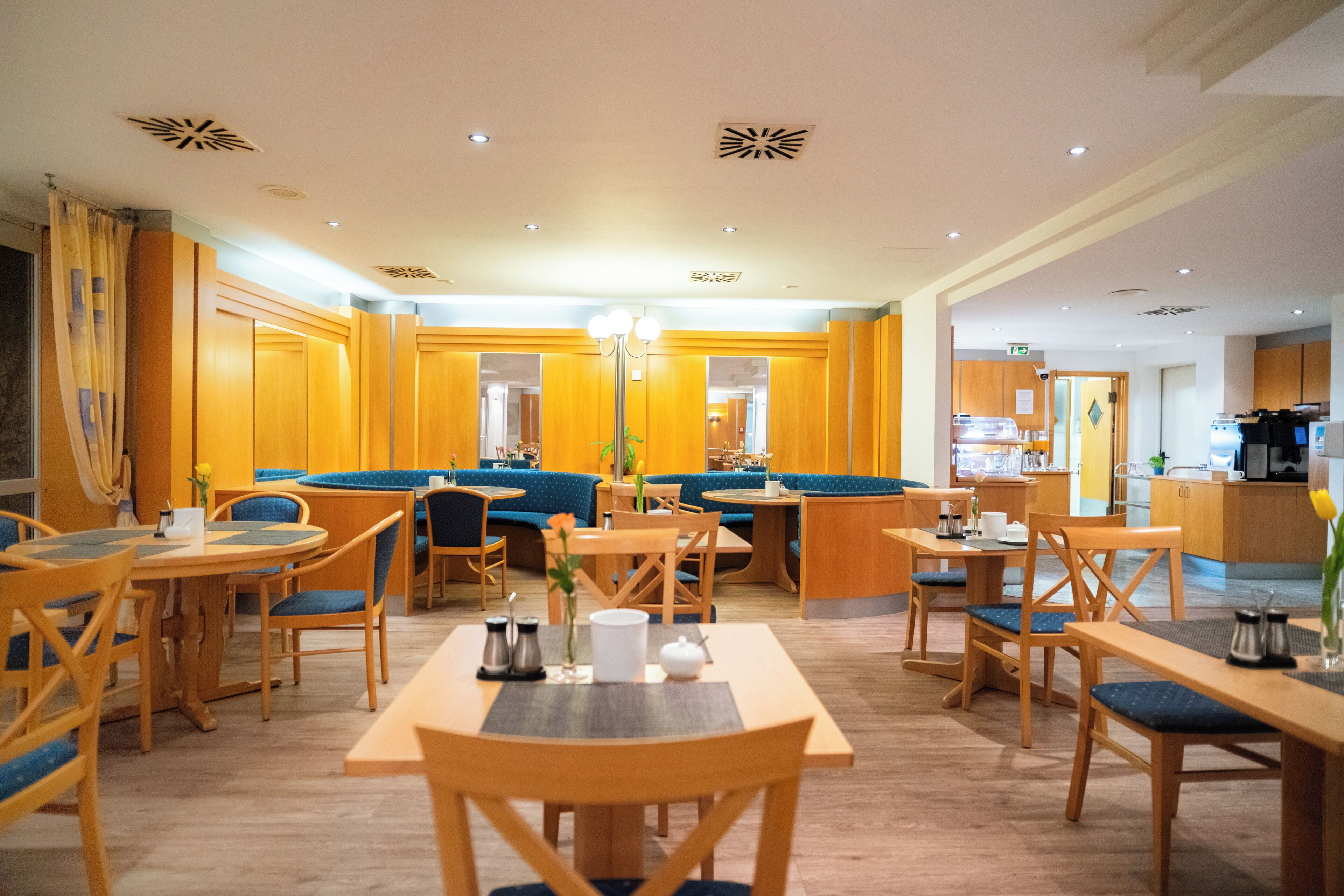 Un vestíbulo de hotel con muebles de madera, zonas de estar y una cocina al fondo.
