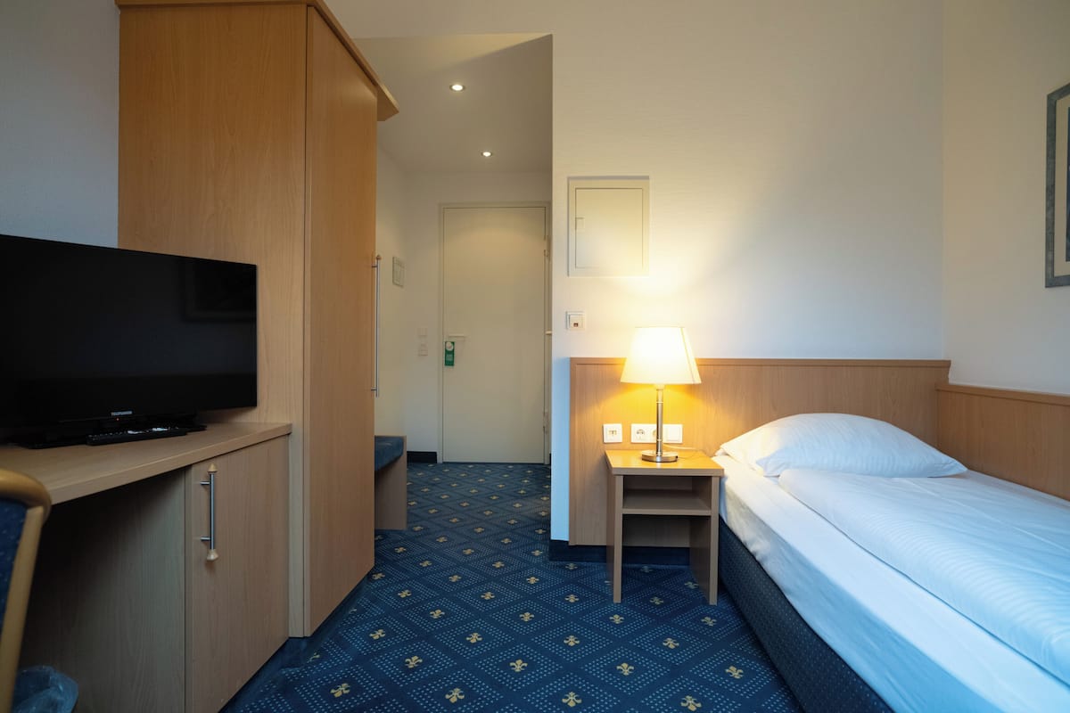 Une chambre d’hôtel avec un lit, un téléviseur posé sur un meuble, une table de chevet avec une lampe et une moquette à motifs.