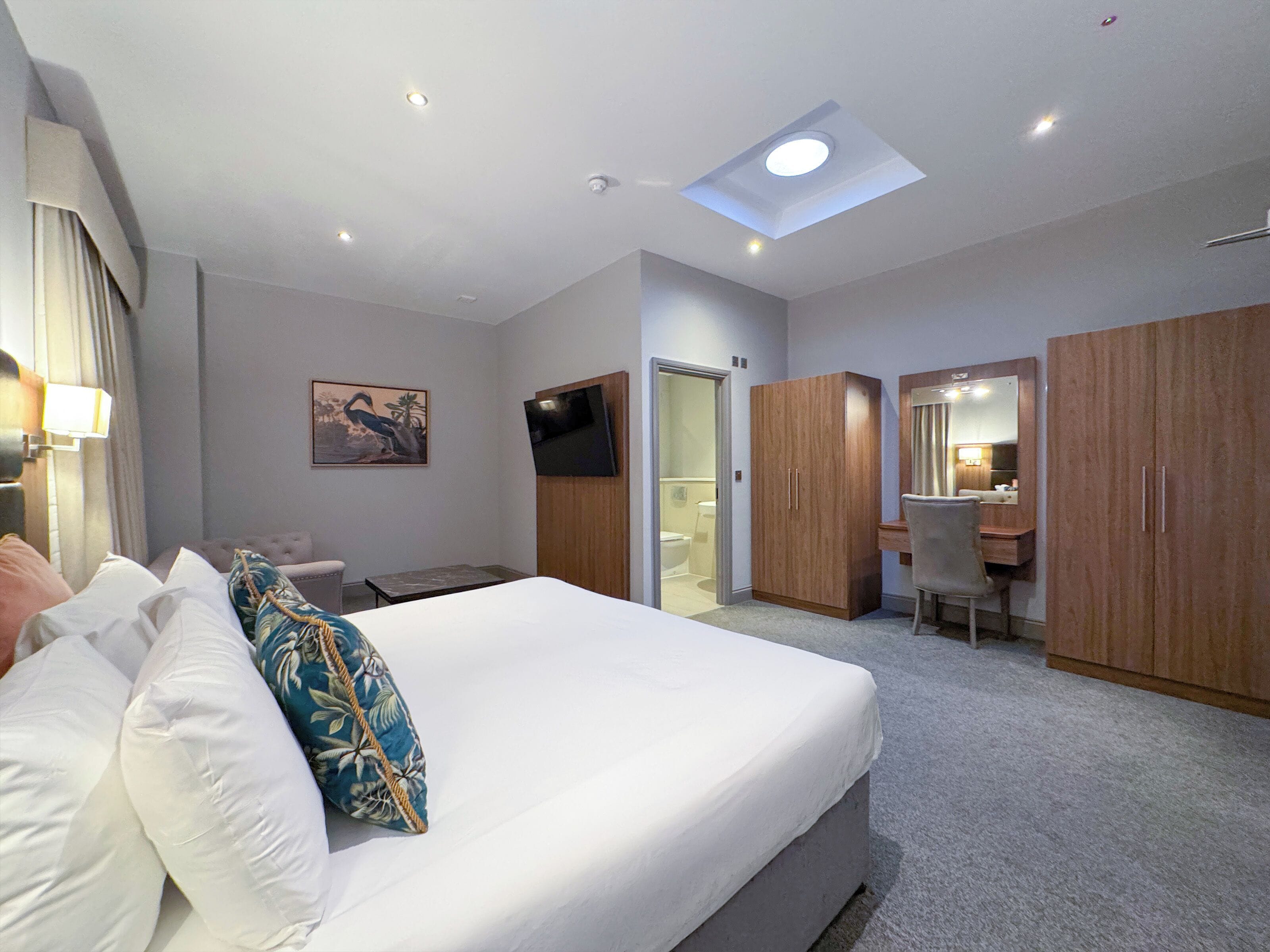 A hotel room with a bed, a desk, a chair, a wardrobe, and a television.