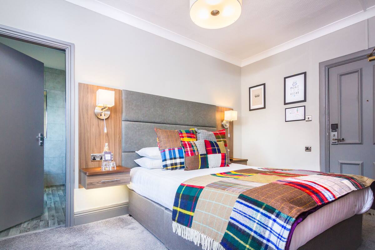 A modern bedroom with a large bed, a nightstand with a lamp, and a wooden headboard.