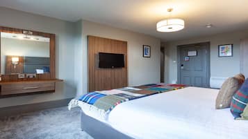 Habitación de hotel con una cama, un televisor de pantalla plana, un armario de madera, un espejo y una puerta con un cartel.