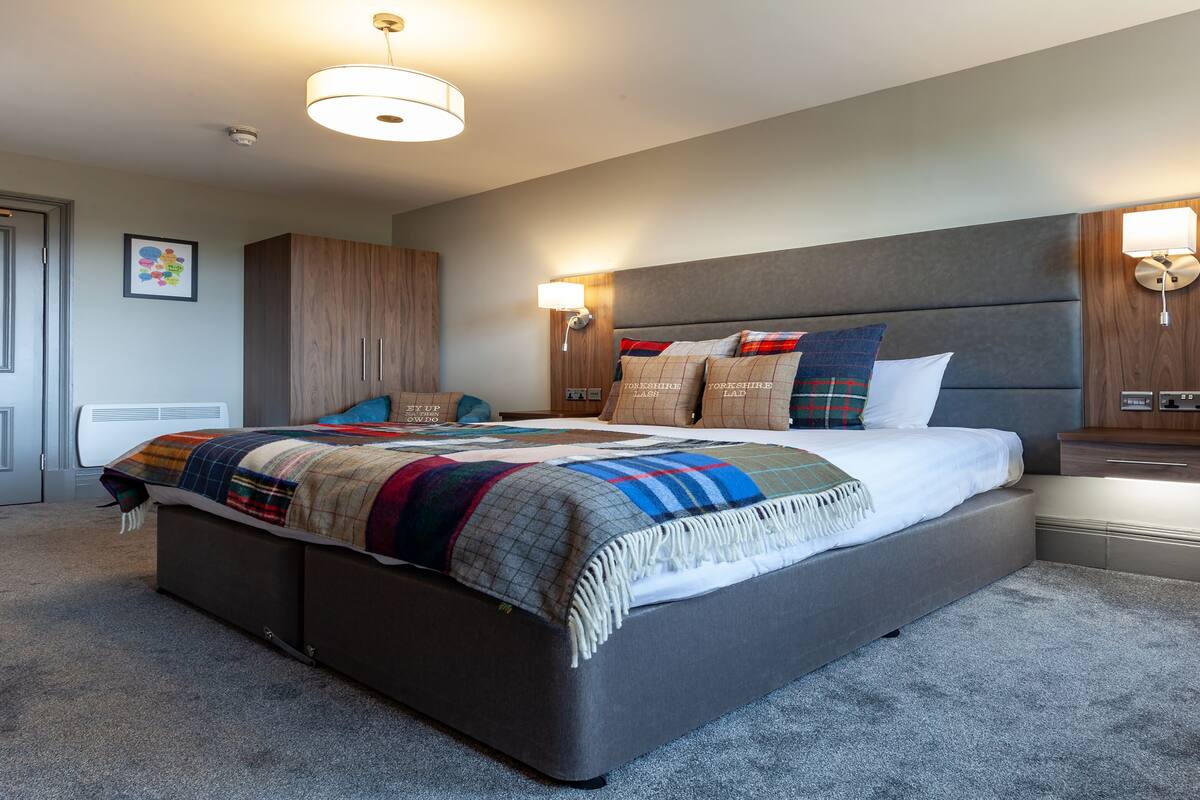 A modern bedroom with a large bed, a wooden wardrobe, and a bedside table with a lamp.