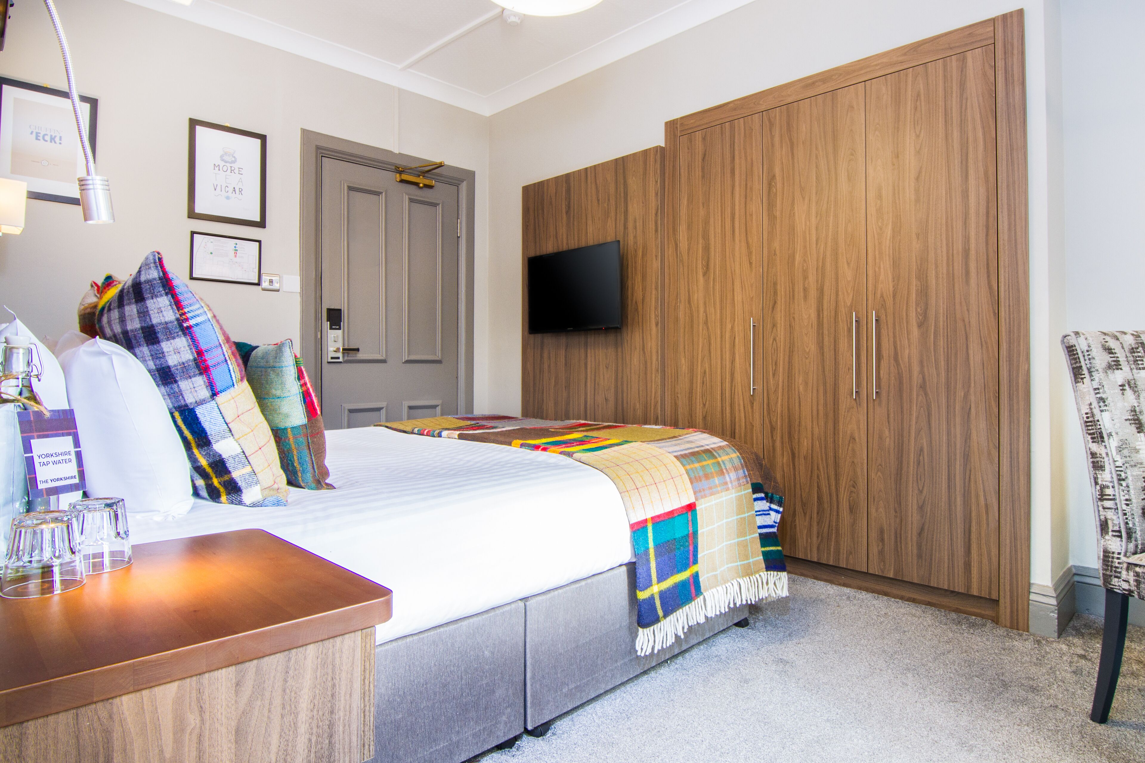 Quarto com cama, guarda-roupa de madeira, televisão na parede e uma cadeira.