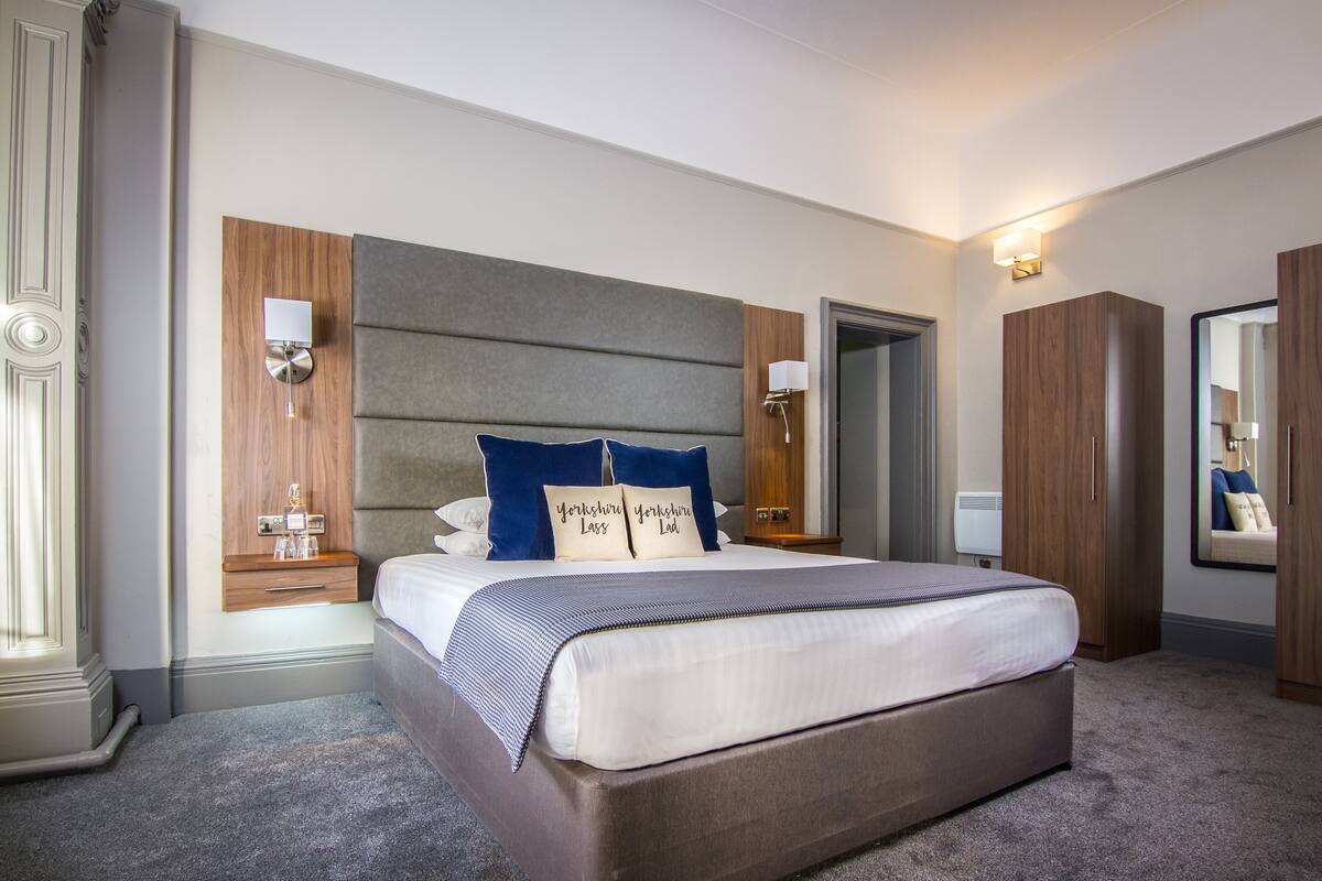 A hotel room with a large bed, a wooden headboard, two bedside tables with lamps, a wardrobe, and a mirror.