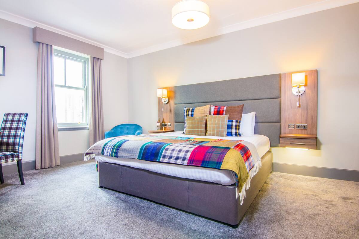 A hotel room with a large bed, a chair, a nightstand, and a window with curtains.
