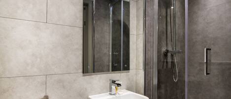 A modern bathroom with a glass-enclosed shower, a white sink, and a large mirror.